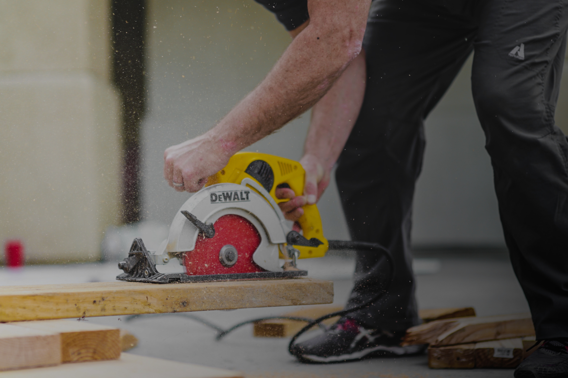 Person skjærer treplank med sirkelsag, sagflis spruter under kapping