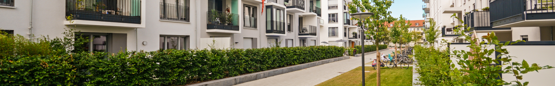 Moderne leilighetsbygg med balkonger, grønn hekk og gangsti mellom husene