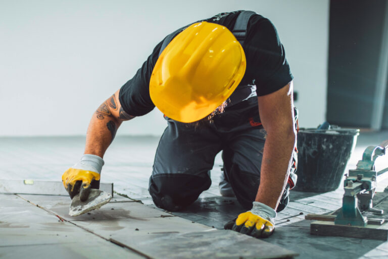 Person med gul vernehjelm legger fliser og bruker sparkelbrett