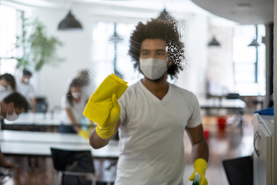 Person rengjør glassflate med gul klut og sprayflaske i kontormiljø