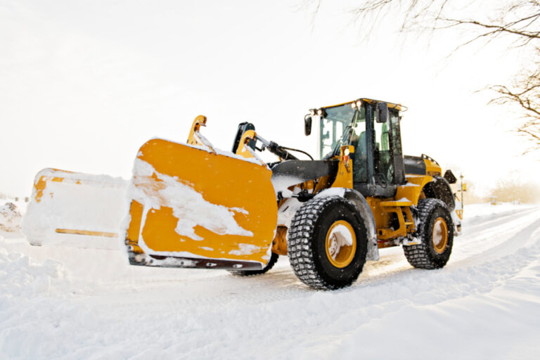 Stor gul hjullaster rydder snø fra vei med frontskuffe