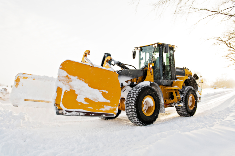 Stor gul hjullaster rydder snø fra vei med frontskuffe