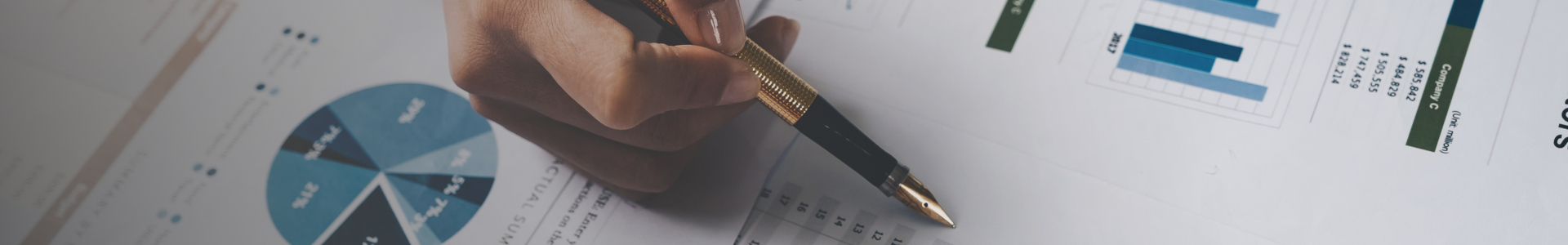 Hånd med penn peker på diagrammer og grafer på papir.