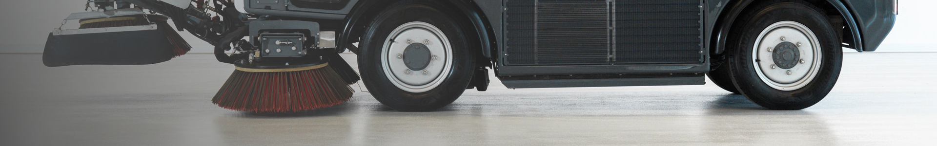Feiemaskin med roterende børster rengjør gulv i stort innendørs område.