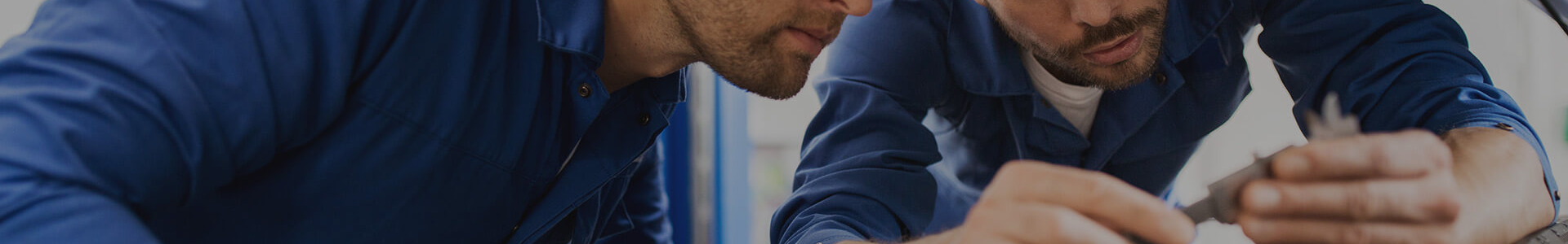 To personer i blå arbeidsklær jobber med en liten metallkomponent.