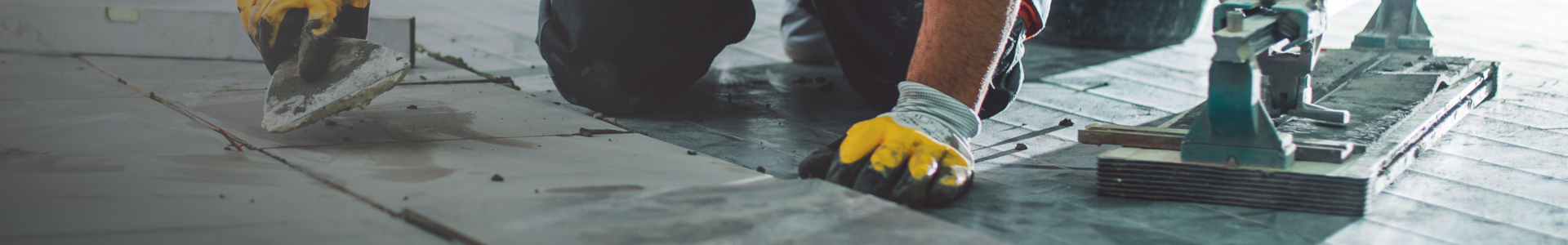 Person med gule hansker legger fliser og påfører fugemasse på gulv.